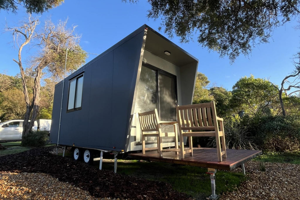 Outdoor view of a modern Transportable Cabin with a wooden deck, nestled among trees, offering a cozy retreat in nature.